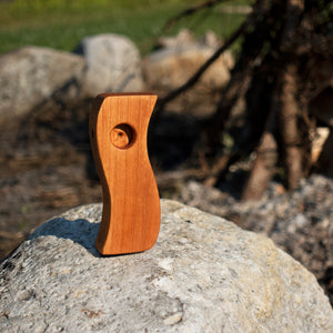 Cherry wood pipe shaped like a tilde resting on top of a rock outdoors